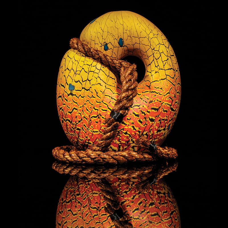 An egg shaped piece of glass artwork, with a rope going through the piece and wrapped around the bottom. by Dan Friday.
